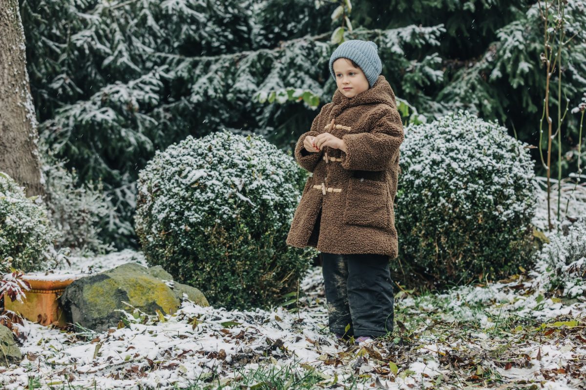 little kid in hat and coat in winter snowy garden e1670336174213