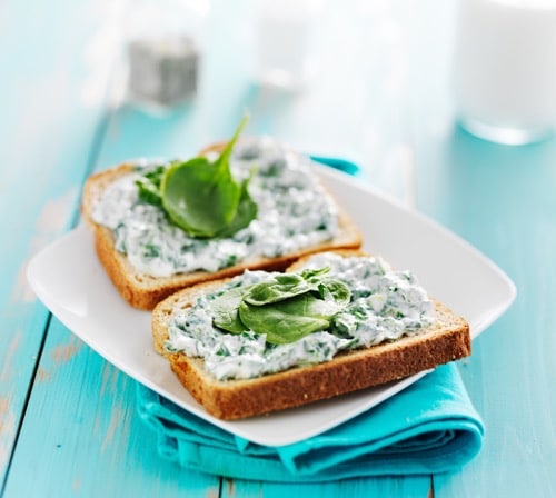 toast with spinach cheese spread on it and leaf garnish