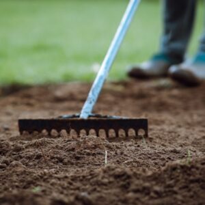 zahradní hrábě v rukou člověka kypřícího půdu stojícího na trávě, úprava půdy